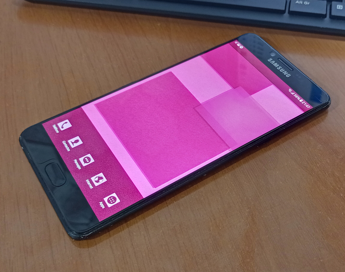 a large phone laying on a table at an angle, the screen is on the home screen and it shows a pink wallpaper with pink icons as well. the phone has 56% of battery and it shows the picture was taken at 21:47